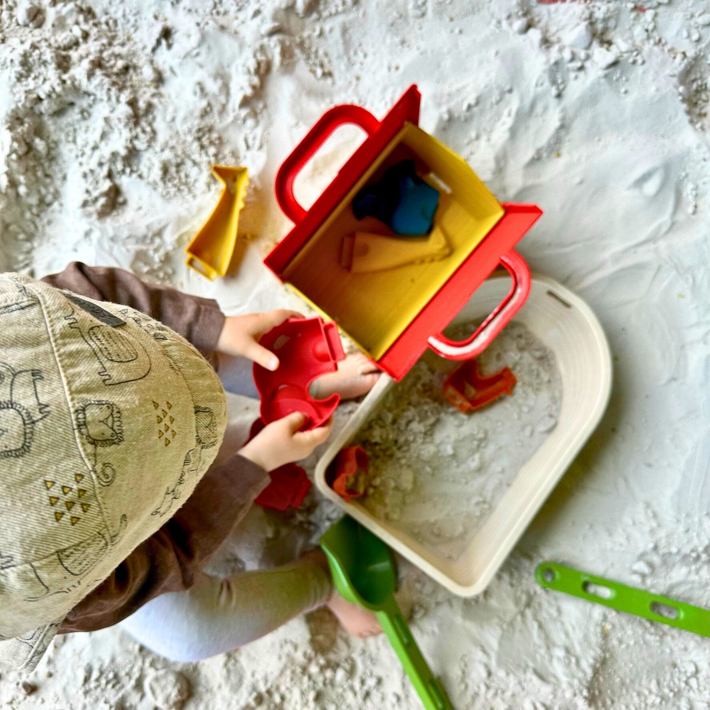 Kind spielt in Sand mit Boot mit aufklappbarem Haus